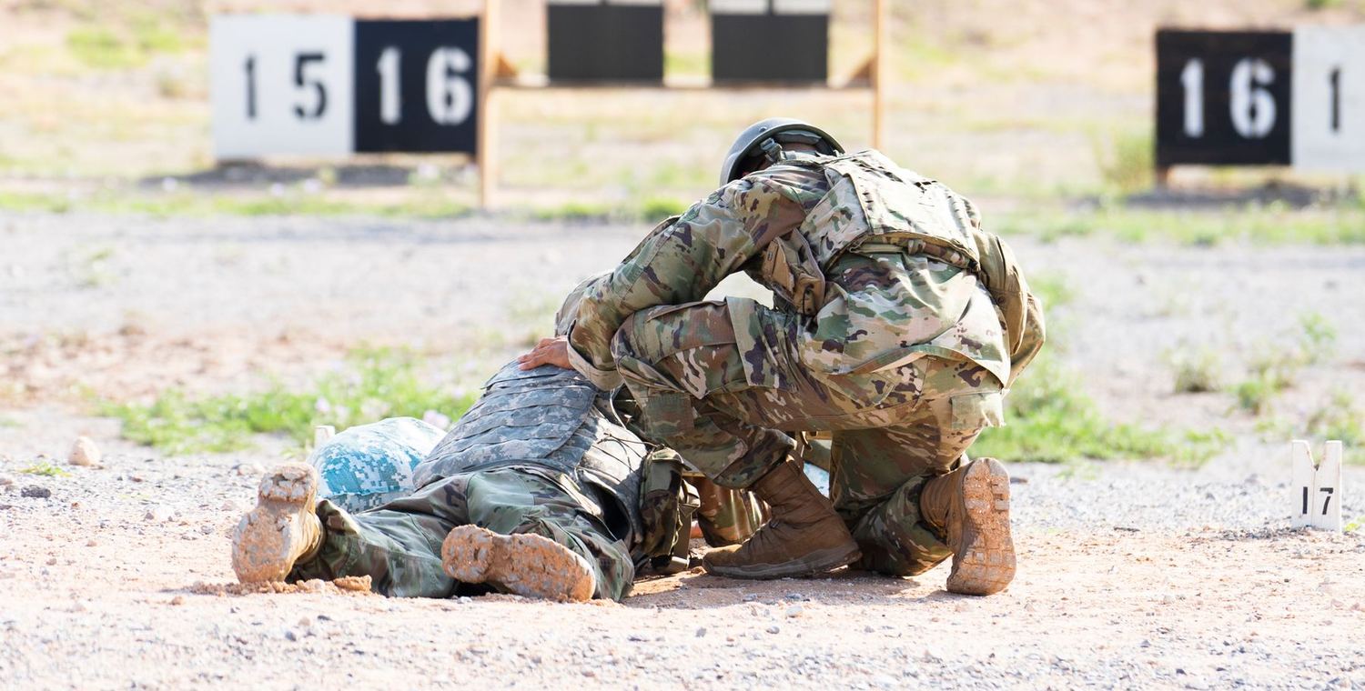 A soldier kneeling over a casualty on the ground during casualty care training